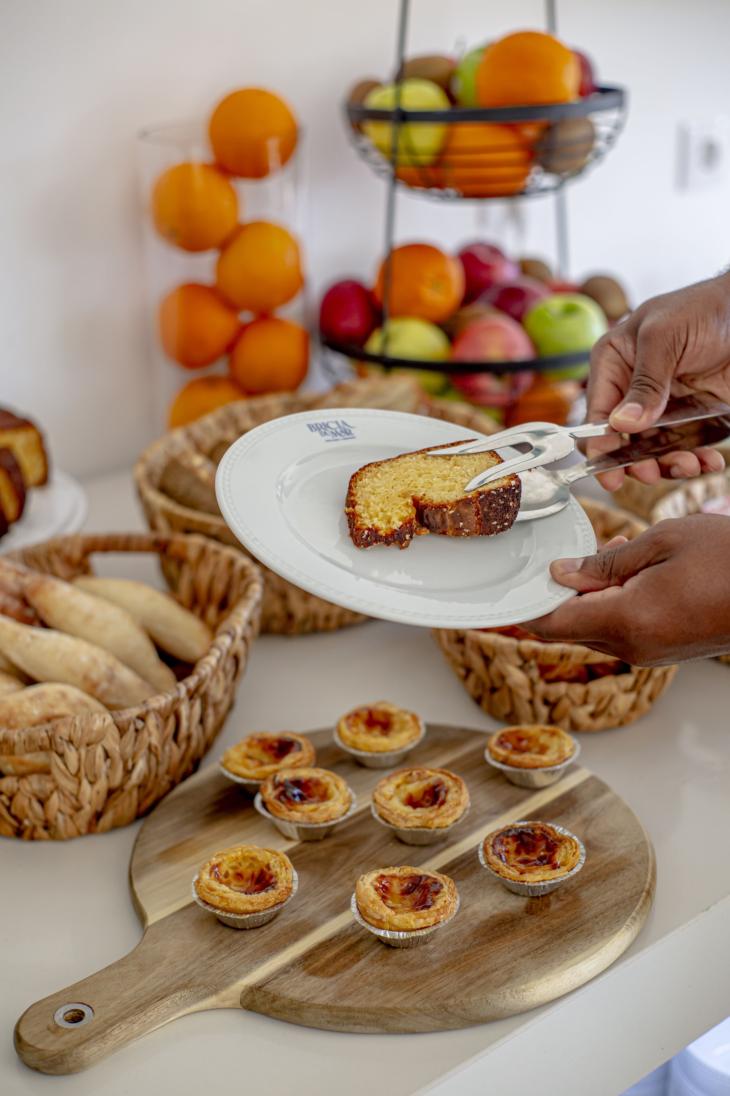 A table with pastries, a plate with a slice of cake, and baskets of bread.