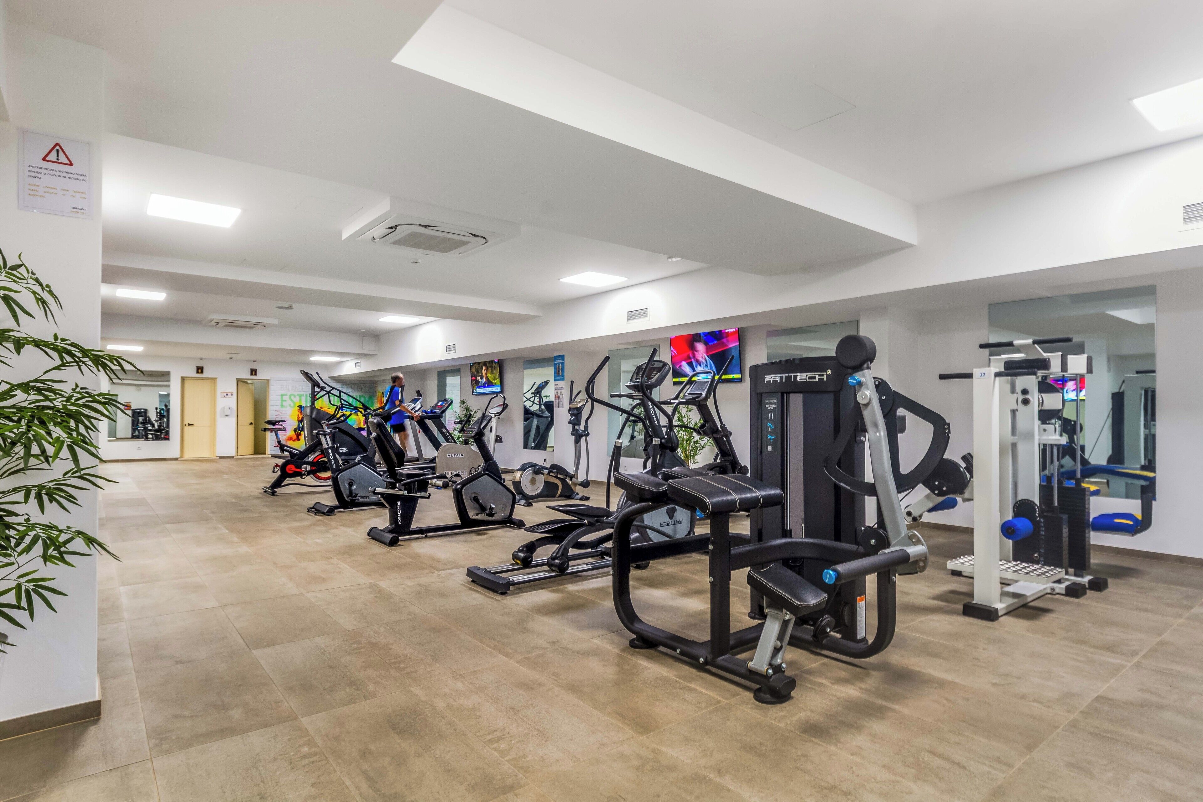 Un gimnasio con diferentes máquinas de ejercicio, un televisor y un espejo.
