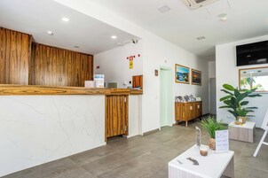 A reception area with a wooden reception desk, a white marble wall, a large potted plant, and a mounted television.
