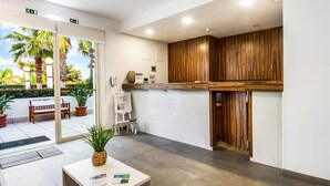 A reception area with a wooden counter, a white reception desk, and a view of a tropical garden outside. - Hotel Rural Brícia du Mar (Lagoa)