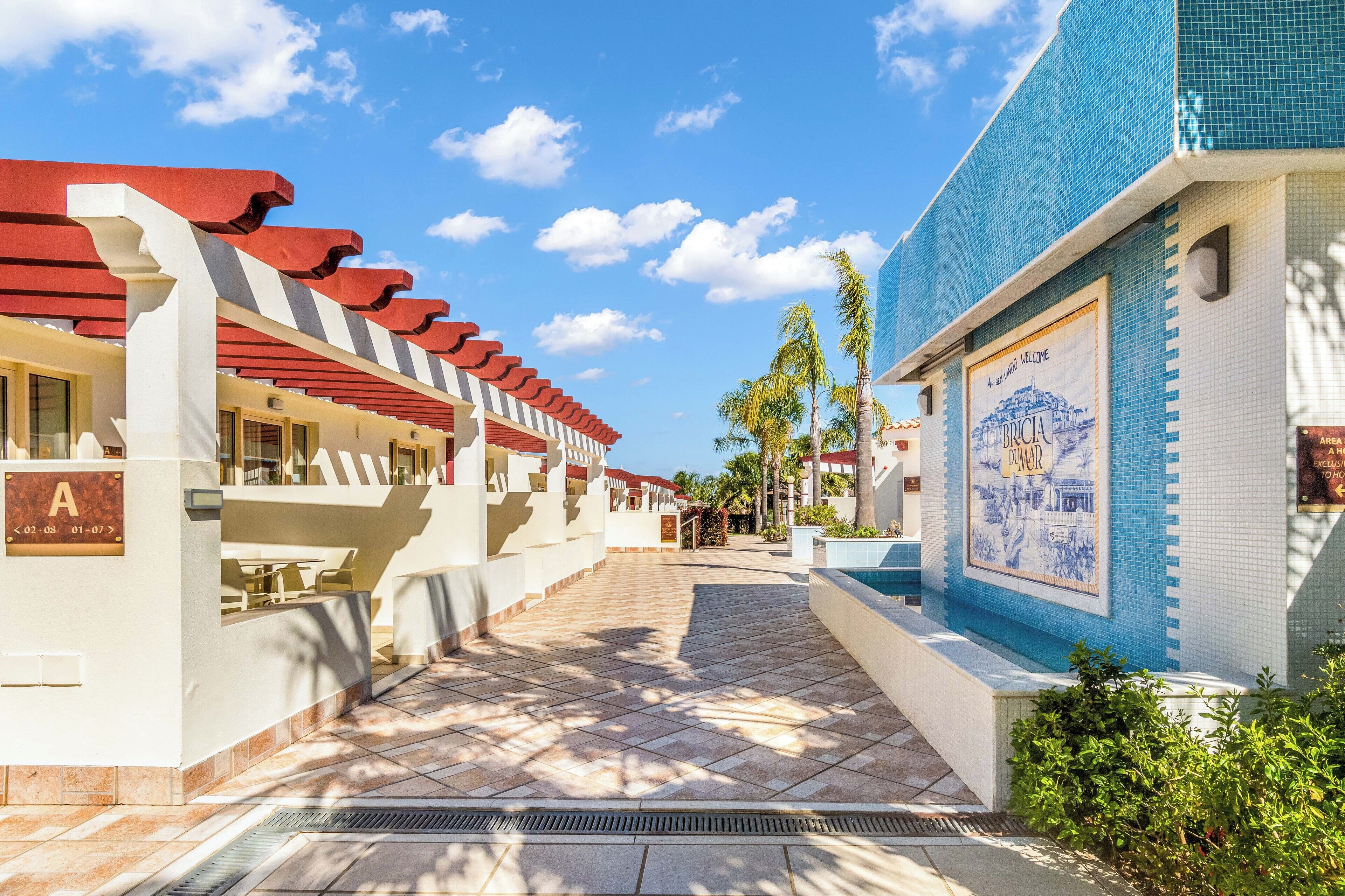 Un pasillo de hotel con piso de baldosas, un toldo rojo y blanco y una pared de mosaico azul.