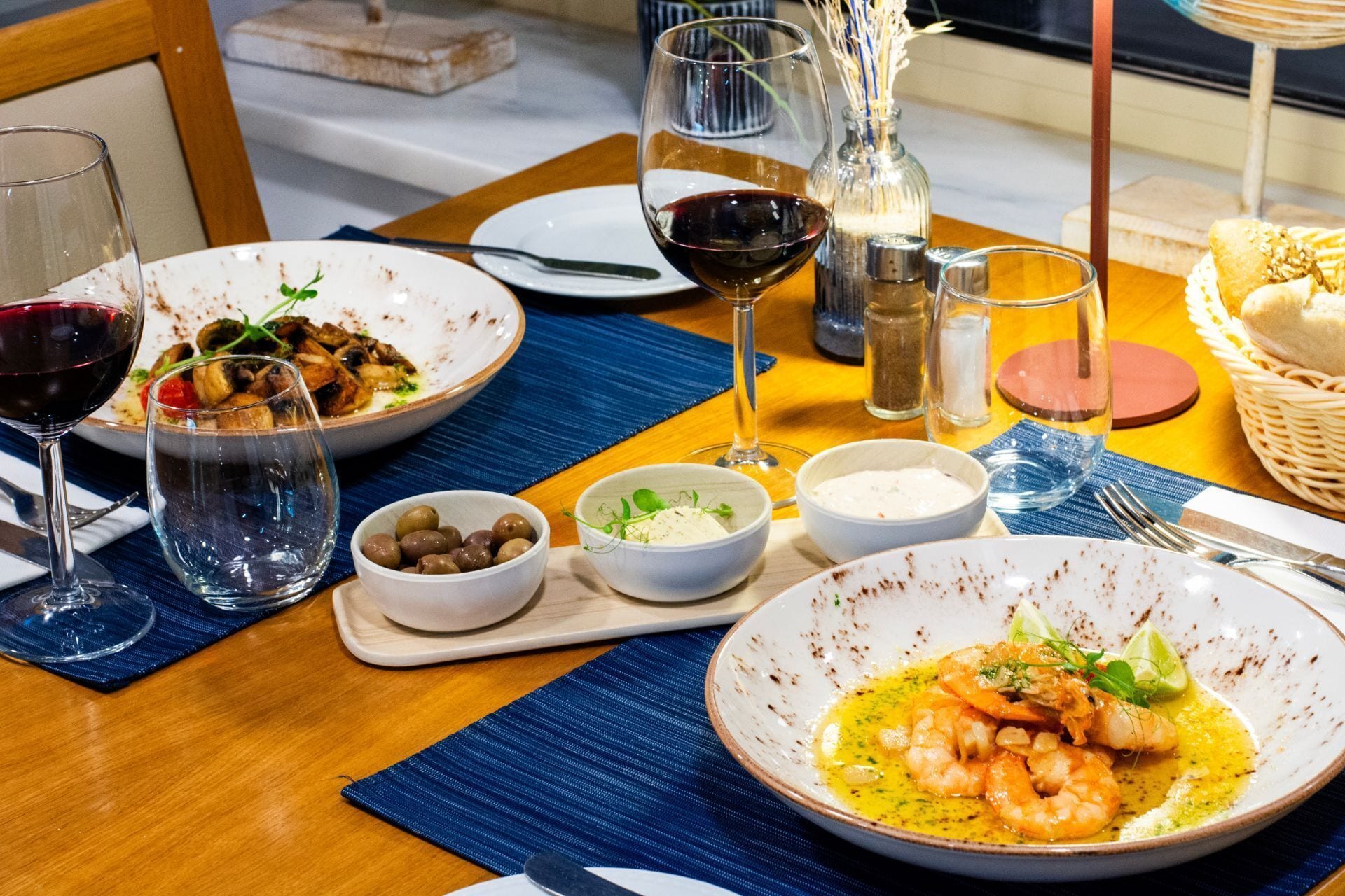 Un tavolo da pranzo imbandito con piatti di cibo, bicchieri di vino e diversi condimenti.