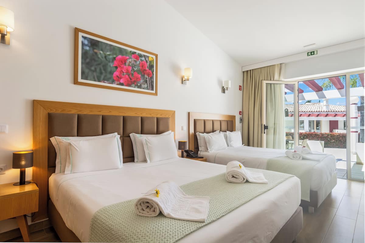 A hotel room with two beds, a painting of flowers on the wall, and a view of the outside.