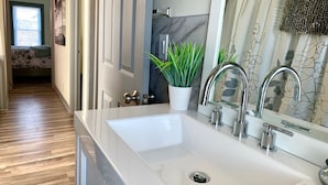 Un baño moderno con un lavamanos blanco, dos grifos, un espejo y una planta en maceta.
