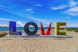 A beach with large letters spelling 'LOVE' made of various materials, a tire, and a blue structure with peeling paint. - Stella Blu - Chesapeake Properties (Cape Charles)