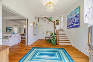 A spacious living area with a staircase, a chandelier, and artwork on the walls. - Stella Blu - Chesapeake Properties (Cape Charles)