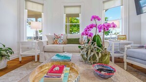 Un salon avec un canapé, une table basse sur laquelle sont posés des livres, une plante en pot et une fenêtre donnant sur un beau paysage.