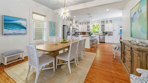 Une cuisine moderne avec des meubles blancs, un îlot central et un coin repas doté de chaises en osier.