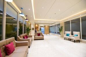 Um hall amplo com um sofá bege, duas poltronas e uma mesa de centro.