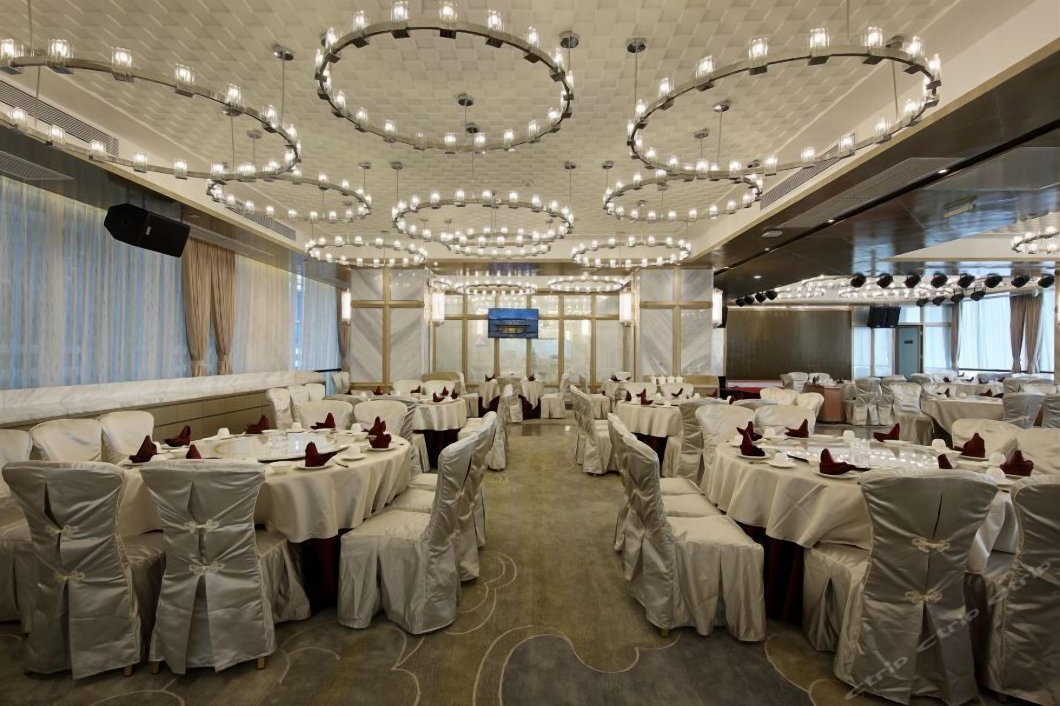 A banquet hall with round tables, white tablecloths, and chairs with white covers.