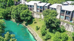 A multi-story building with balconies, surrounded by lush greenery and a body of water.