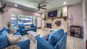 A living room with blue sofas, a fireplace, a ceiling fan, and a TV mounted on the wall.