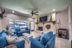 A living room with blue sofas, a fireplace, a ceiling fan, and a TV mounted on the wall.