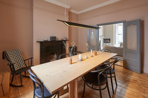 Un comedor con una mesa de madera, sillas negras, chimenea y una lámpara colgante moderna.