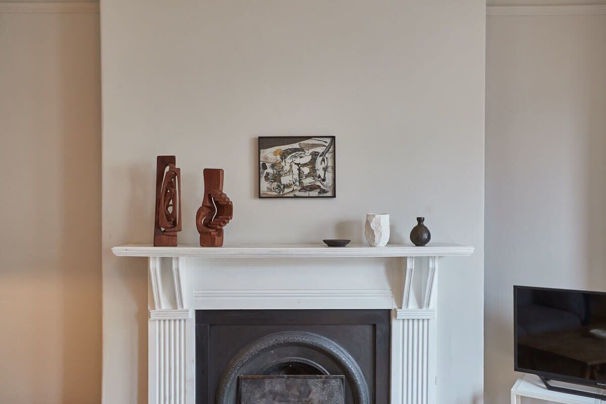 A fireplace with a mantel displaying three vases and a framed artwork.