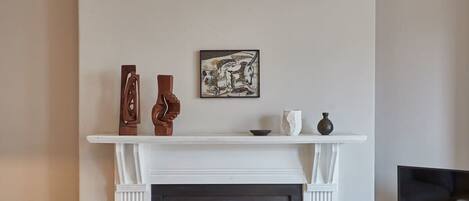 A fireplace with a mantel displaying three vases and a framed artwork.