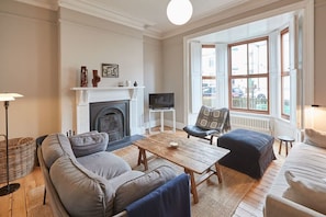 A living room with a fireplace, a television, and a large window with a view of the street.