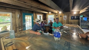 Un coin bar rustique avec des poutres en bois, une grande table en verre et quelques clients.