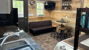 Une pièce confortable, aménagée comme un chalet, avec un canapé, une petite table ronde et un coin bar avec des tabourets.