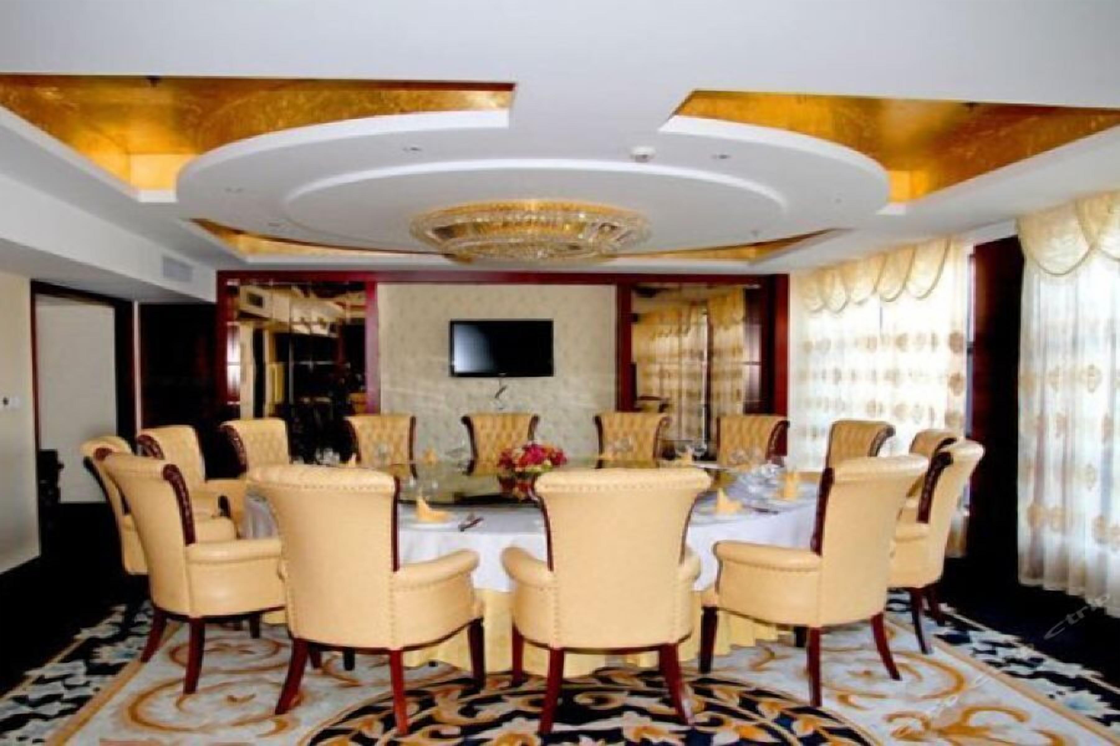 A formal dining room with a round table, six chairs, a chandelier, and a flat-screen TV on the wall.