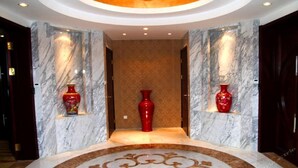 A marble-floored hallway with two red vases on shelves, a central red vase, and a circular patterned area in the middle. - Beijing Huihao International Hotel (Beijing)
