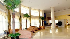 A spacious lobby with a modern design, featuring a seating area with sofas and chairs, large windows with curtains, and several palm trees. - Beijing Huihao International Hotel (Beijing)