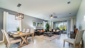 A modern living room with a dining area, featuring a large window, ceiling fan, and a view of the outdoors. - Solterra Resort Pool & Spa, Games Room, Lake View & Extensive Resort Amenities (Davenport)