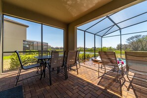 Une terrasse couverte avec une table et des chaises, de grandes fenêtres et une vue sur un lac et des maisons.