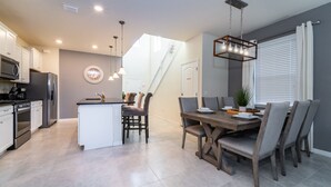 A modern kitchen with a central island, dining table with chairs, and a staircase leading to an upper level. - Solterra Resort Pool & Spa, Games Room, Lake View & Extensive Resort Amenities (Davenport)