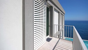 Ένα μπαλκόνι με θέα στον ωκεανό, μια πισίνα και ένα κτίριο με λευκά παντζούρια.