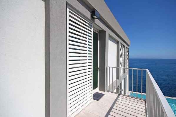 Un balcon avec vue sur l’océan, une piscine et un bâtiment aux volets blancs.