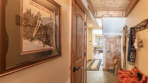 A hallway with a framed picture of a skier, wooden doors, a doghouse, and a red sofa with patterned cushions. - Beautiful Mountain 2 Bedroom Ski-In/Ski-Out in Ski Trails by RedAwning Save 10% on 3 Nights, 15% on 5 Nights! (Truckee)