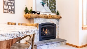 A cozy room with a stone fireplace, a wooden table, and a framed picture of a skier. - Beautiful Mountain 2 Bedroom Ski-In/Ski-Out in Ski Trails by RedAwning Save 10% on 3 Nights, 15% on 5 Nights! (Truckee)