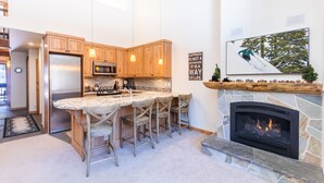 A modern kitchen with a central island, wooden cabinets, and a stone fireplace. - Beautiful Mountain 2 Bedroom Ski-In/Ski-Out in Ski Trails by RedAwning Save 10% on 3 Nights, 15% on 5 Nights! (Truckee)