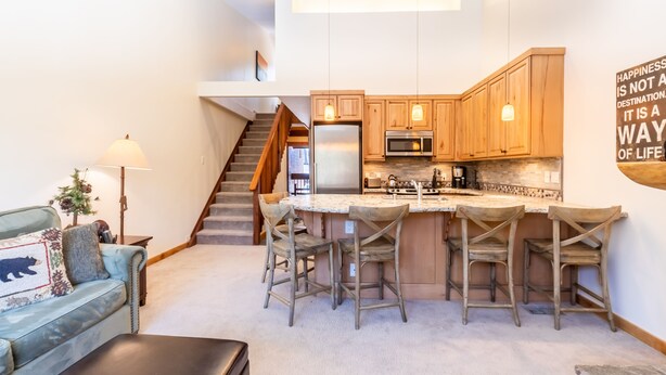 A modern kitchen with wooden cabinets, a central island with bar stools, a built-in oven, and a microwave. A staircase leads to an upper level. - Beautiful Mountain 2 Bedroom Ski-In/Ski-Out in Ski Trails by RedAwning Save 10% on 3 Nights, 15% on 5 Nights! (Truckee)