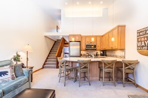 A modern kitchen with wooden cabinets, a central island with bar stools, a built-in oven, and a microwave. A staircase leads to an upper level. - Beautiful Mountain 2 Bedroom Ski-In/Ski-Out in Ski Trails by RedAwning Save 10% on 3 Nights, 15% on 5 Nights! (Truckee)