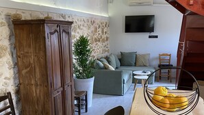 Ein gemütlicher Wohnbereich mit einer Holztreppe, einer Steinwand, einem großen Schrank, einer Couch, einem Couchtisch und einer Obstschale.
