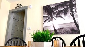 A dining area with a table set for two, a potted plant, and a wall-mounted picture of a beach scene.