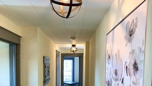 A hallway with wooden flooring, a ceiling light fixture, and a large floral artwork on the wall.