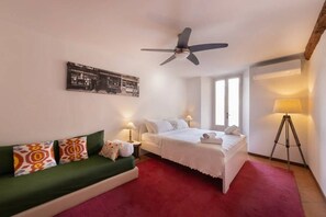 A hotel room with a bed, a green sofa, a ceiling fan, a lamp, and a wall-mounted picture. - Italian Lakes 2 bedroom Apartment with fresco (Lesa)