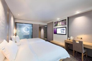 A hotel room with a large bed, a desk with a chair, a TV mounted on the wall, and a window with a view of the city. - Lavande Hotel (Chengdu)