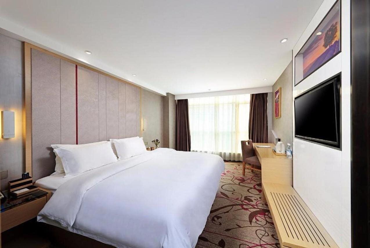 A hotel room with a large bed, a desk, a TV, and a window with curtains.