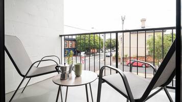 A balcony with two chairs, a small table, and a view of a street with cars and buildings.