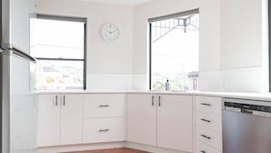 Una cocina moderna con armarios blancos, lavavajillas y dos ventanas que dejan entrar luz natural.