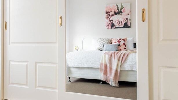 Un dormitorio con un espejo grande, una cama con edredón blanco y una obra de arte floral en la pared.