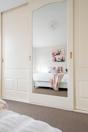 A bedroom with a large mirror, a bed with a white comforter, and a floral artwork on the wall. - CBD Central Hub | Parking & WiFi (Launceston)