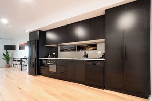 A modern kitchen with dark cabinetry, a wooden countertop, and a built-in oven. - Central & Modern Inner City Apartment with WiFi (Launceston)