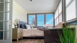 Een moderne slaapkamer met een bed, nachtkastje en een groot raam met jaloezieën.