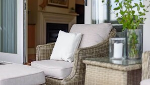 A wicker chair with a cushion, a glass table with a candle, and a plant. - Lakeside Suite 1 + Lakeside Retreat + Spa Bath (Daylesford)