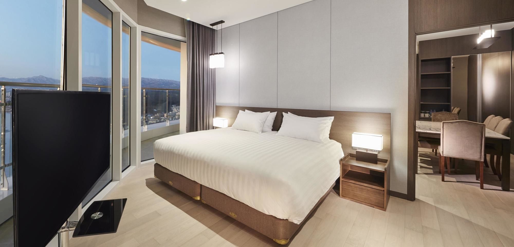 A modern hotel room with a large bed, bedside tables, a TV, and a city view.